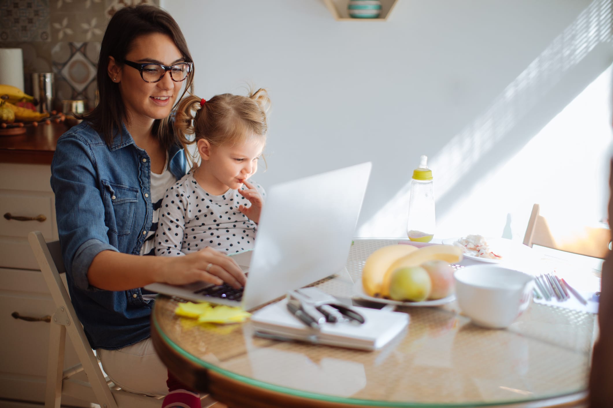 A woman with her daughter on her lap working on her laptop.