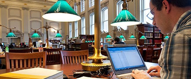 A man on his laptop sitting at a table at the campus library