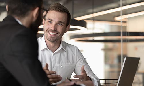Close up of happy Caucasian middle-aged businessman talk with male colleague working together using laptop, smiling man employee speak discussing ideas with man coworker