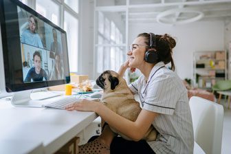 Woman having a video call with colleagues while sitting in an office setting with a pug on her lap