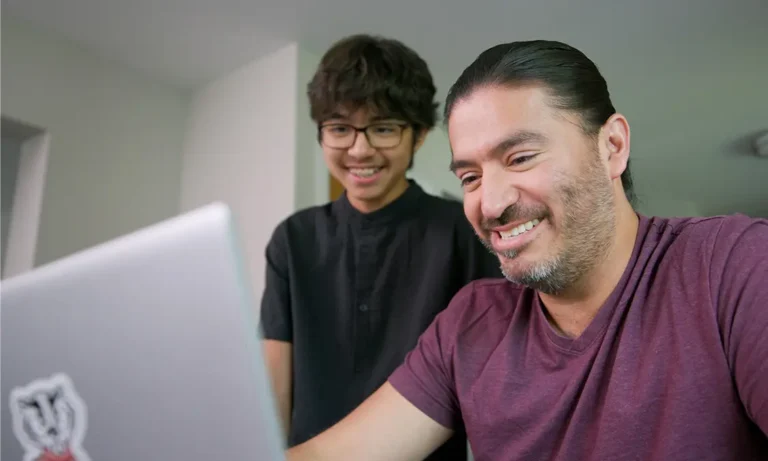 A smiling Manny and his son working on a laptop