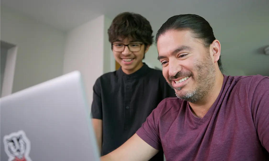 Manny Avila on his computer while his son looks over his shoulder