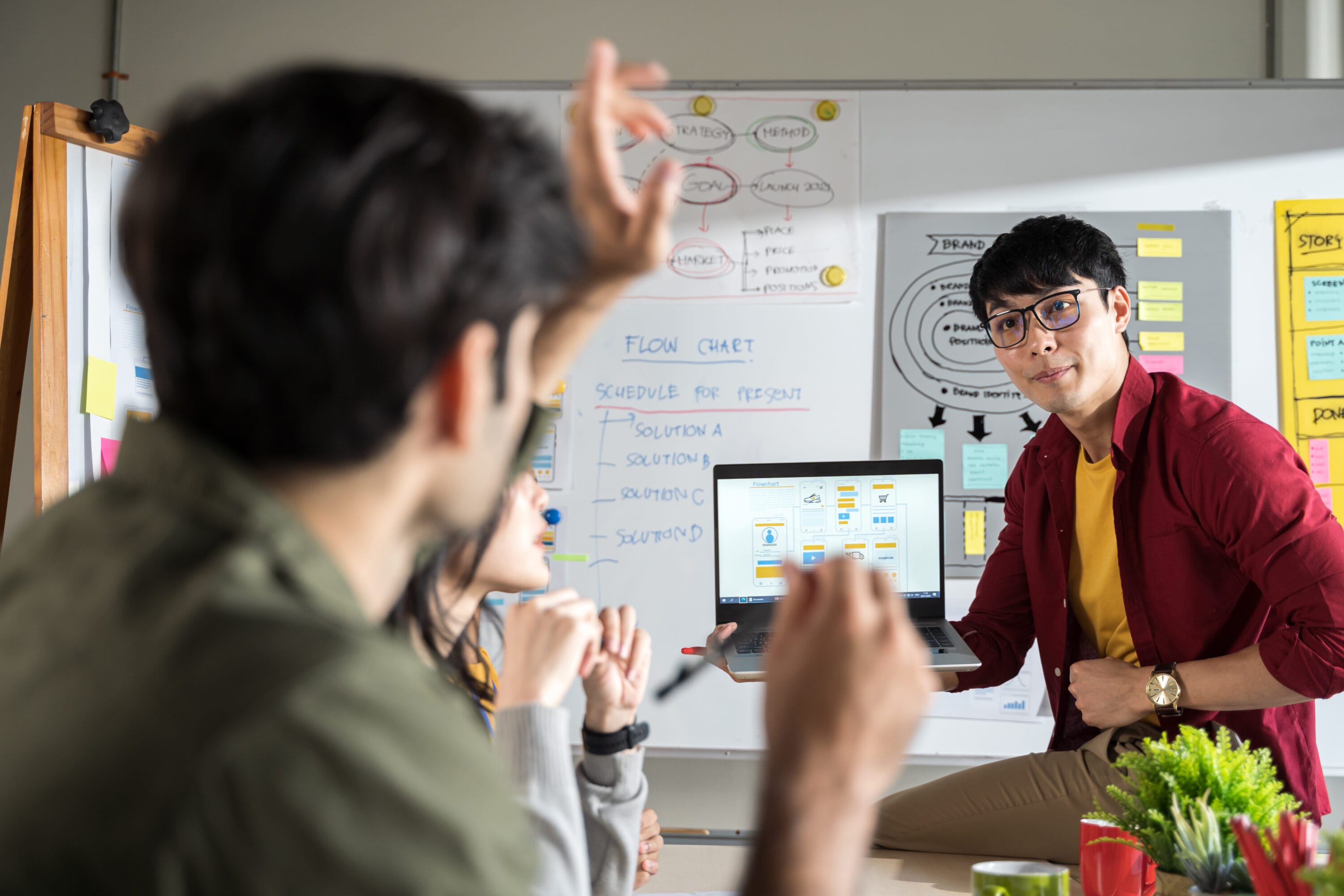 A young man holding a laptop in front of a team of designers.