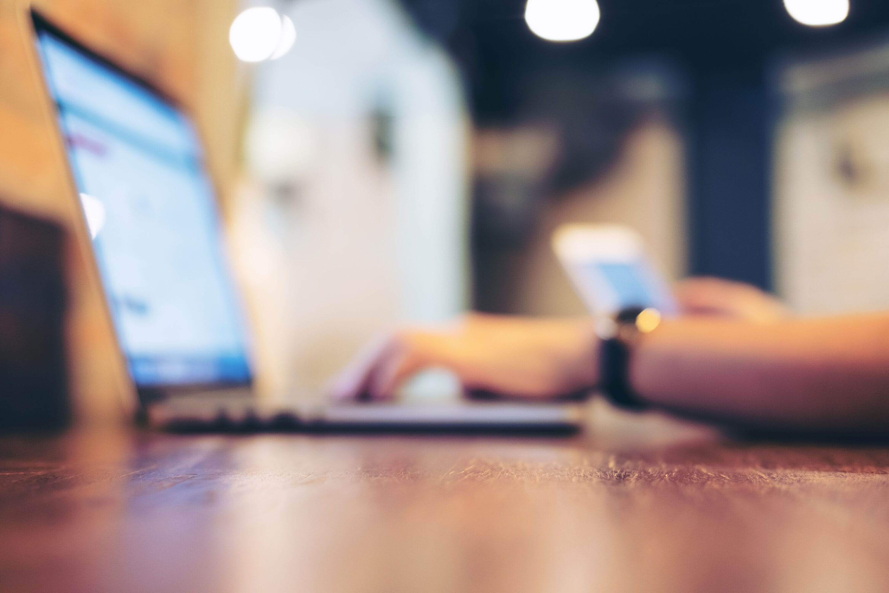 Image of a pair of hands working on a laptop while scrolling on their phone.