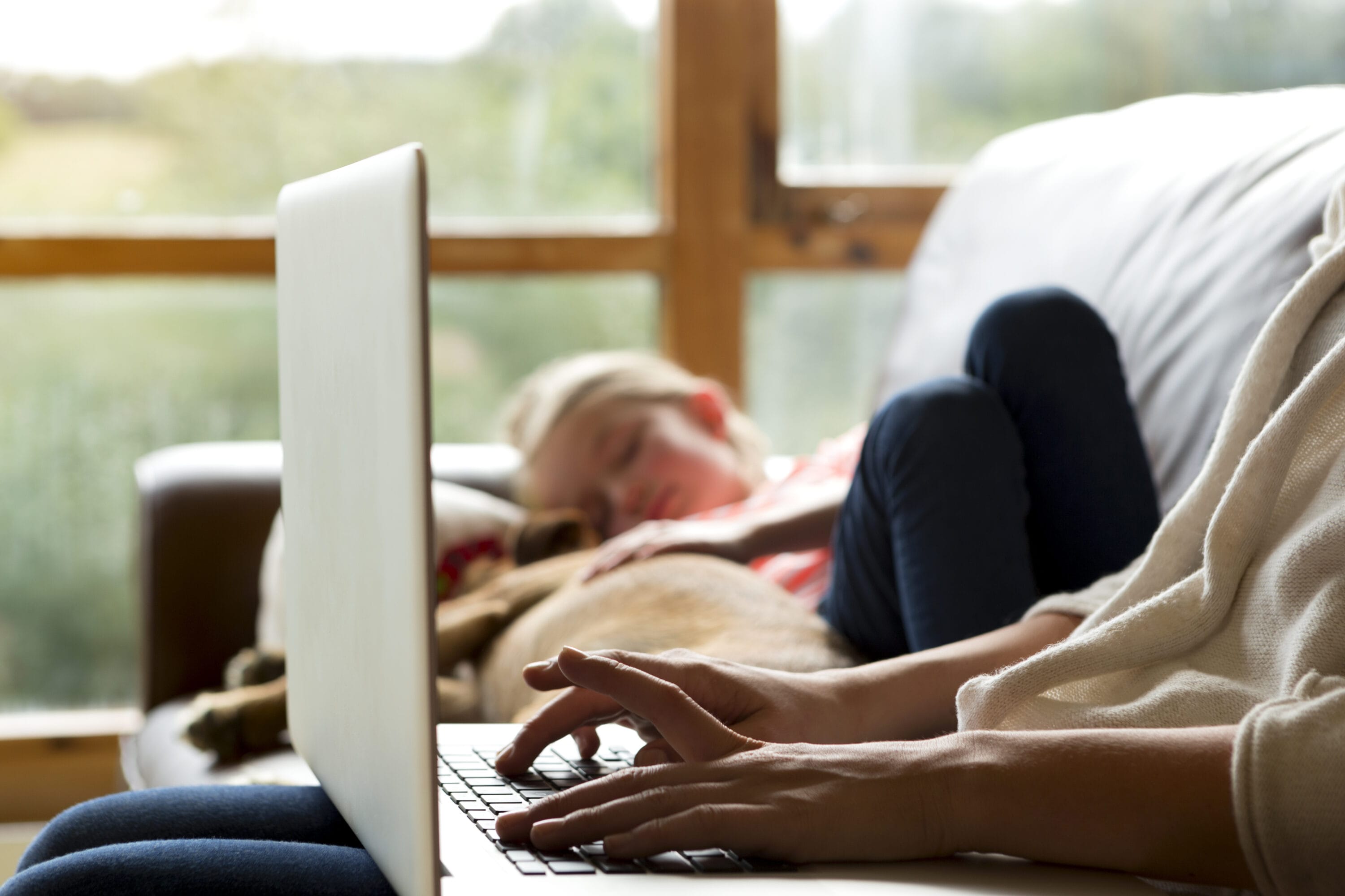 An image of a pair of hands typing on the keyboard while a child sleeps in the background.