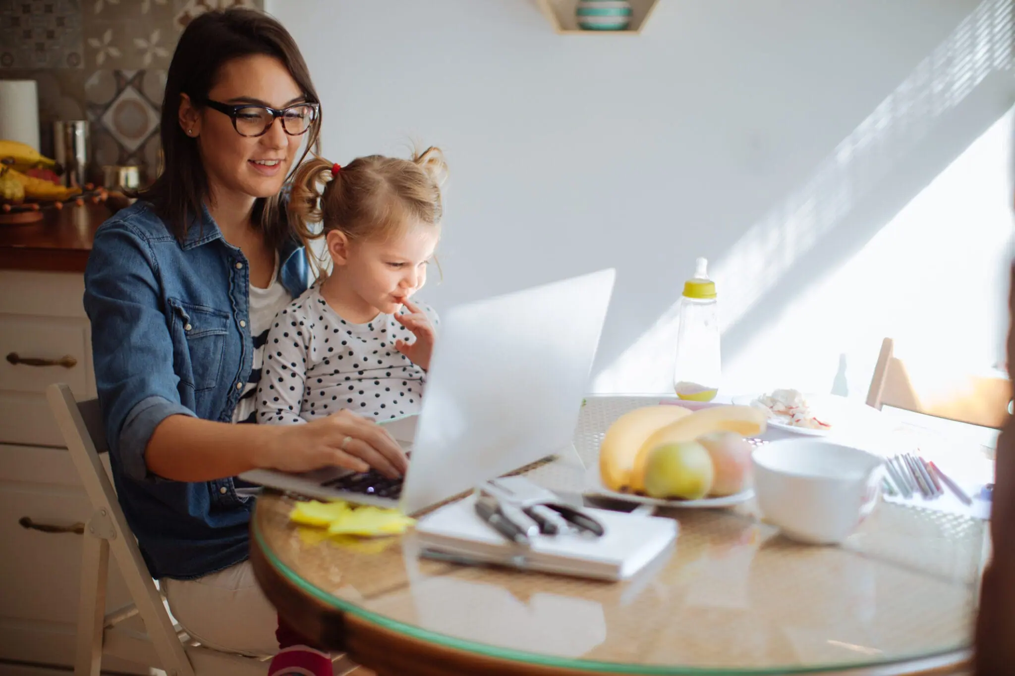 A woman with her daughter on her lap working on her laptop.