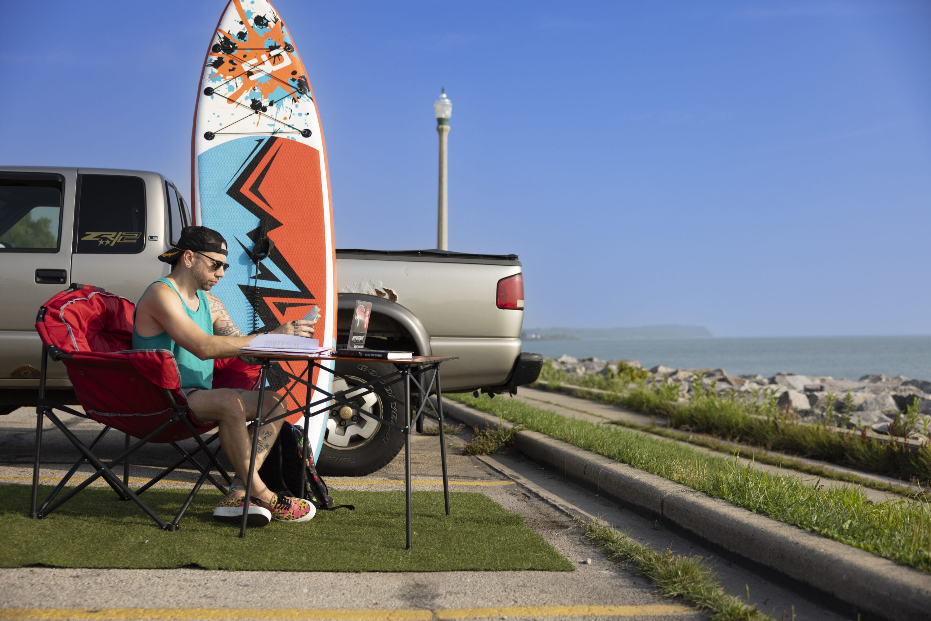 Joey Nicgorski working in front of a lake beside his surfboard.