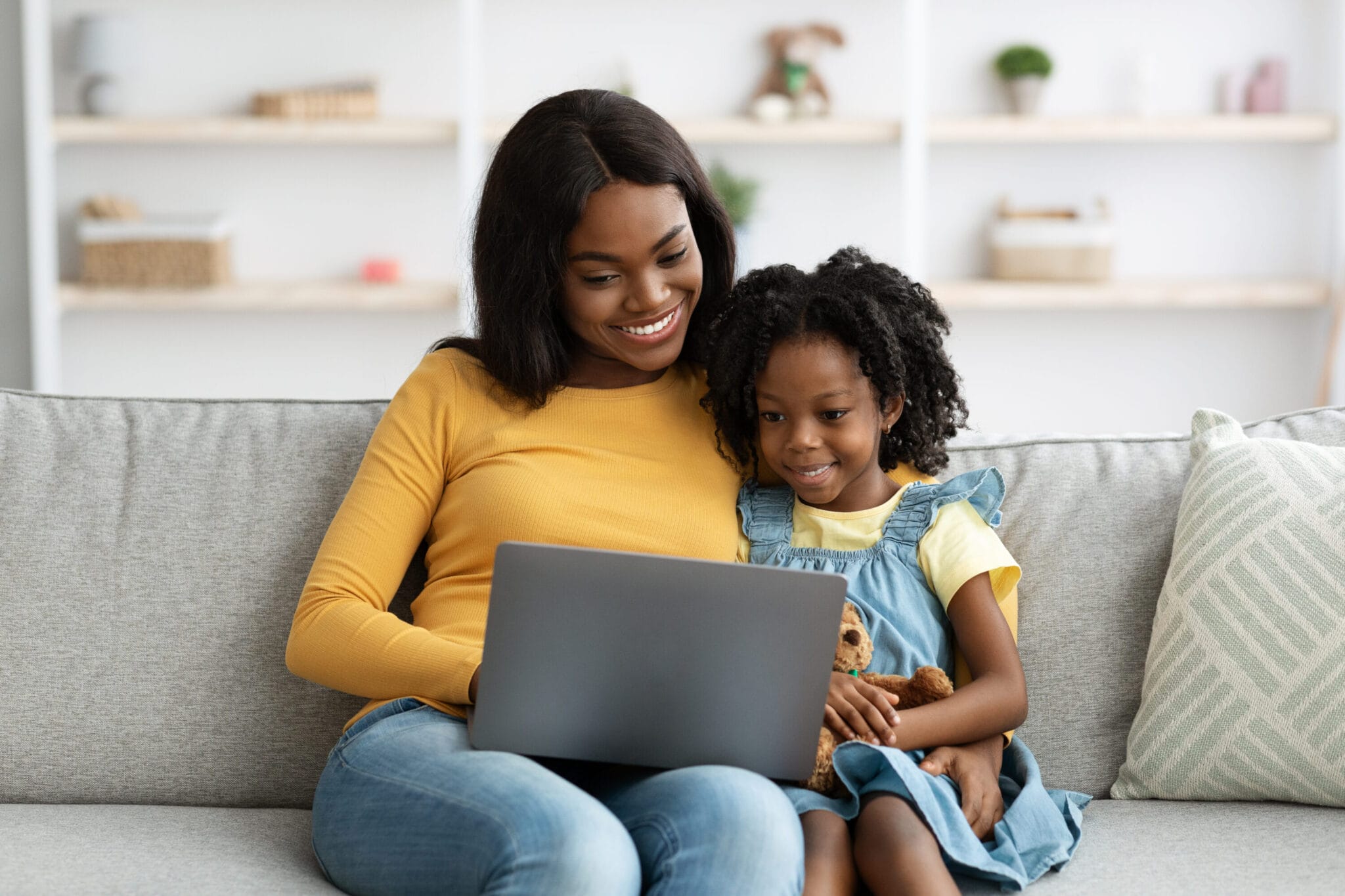 A woman sitting beside her daughter as they scroll through a laptop together.