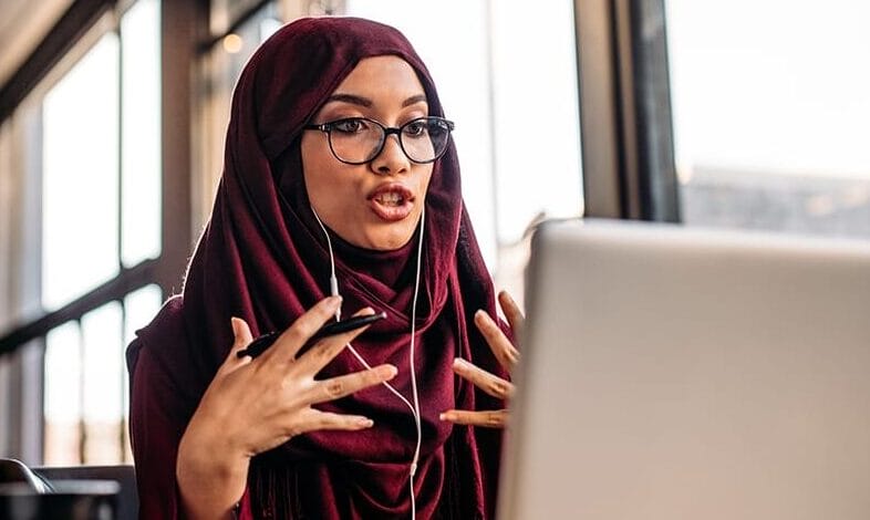 A woman in hijab having a video chat on laptop while sitting at coffee shop.