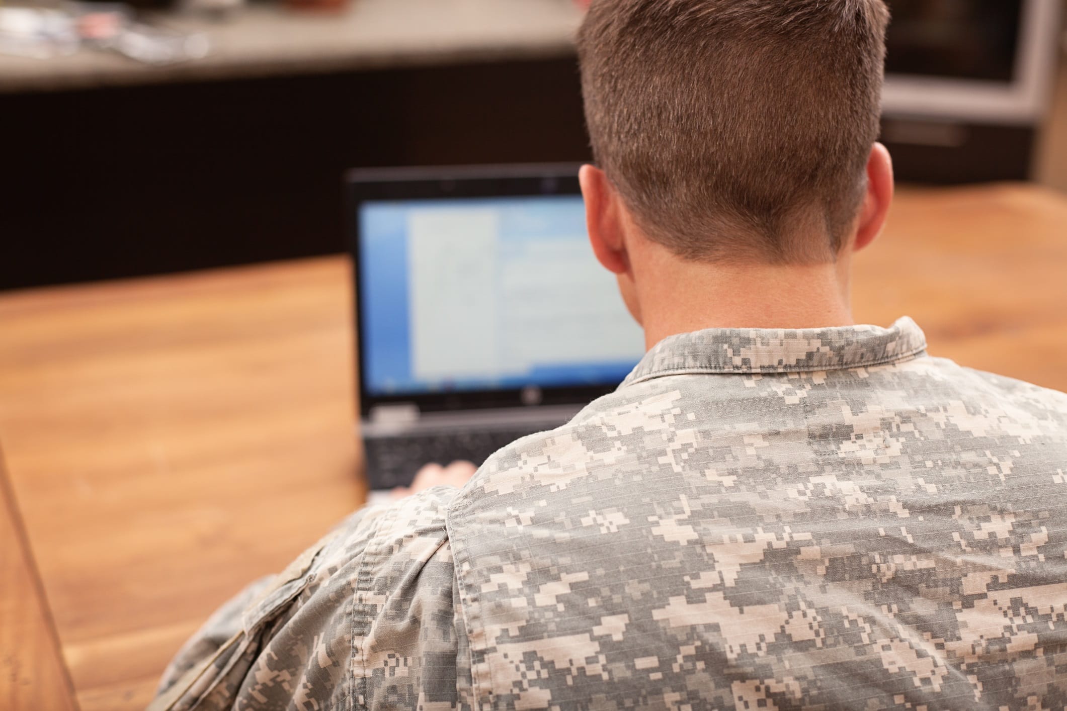 The back of a man with his military uniform on, working on his computer